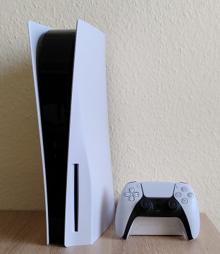 Bild: PS5 Konsole hochkant mit Dualsense Controller: Der Controller wirkt gegenüber der Konsole regelrecht klein, ist aber genauso groß wie früher. Hochkant ist zudem nicht meine präferierte Ausrichtung